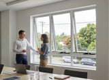 Two people shaking hands in an office with large windows showing a view of cars outside.